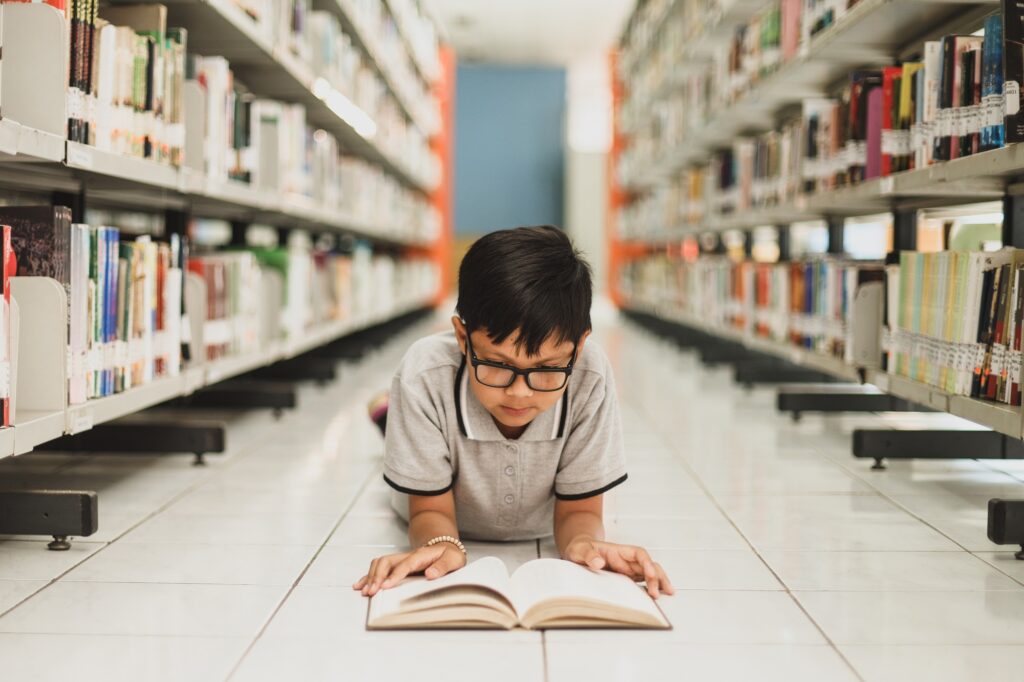 Smart school boy reading a book at the library